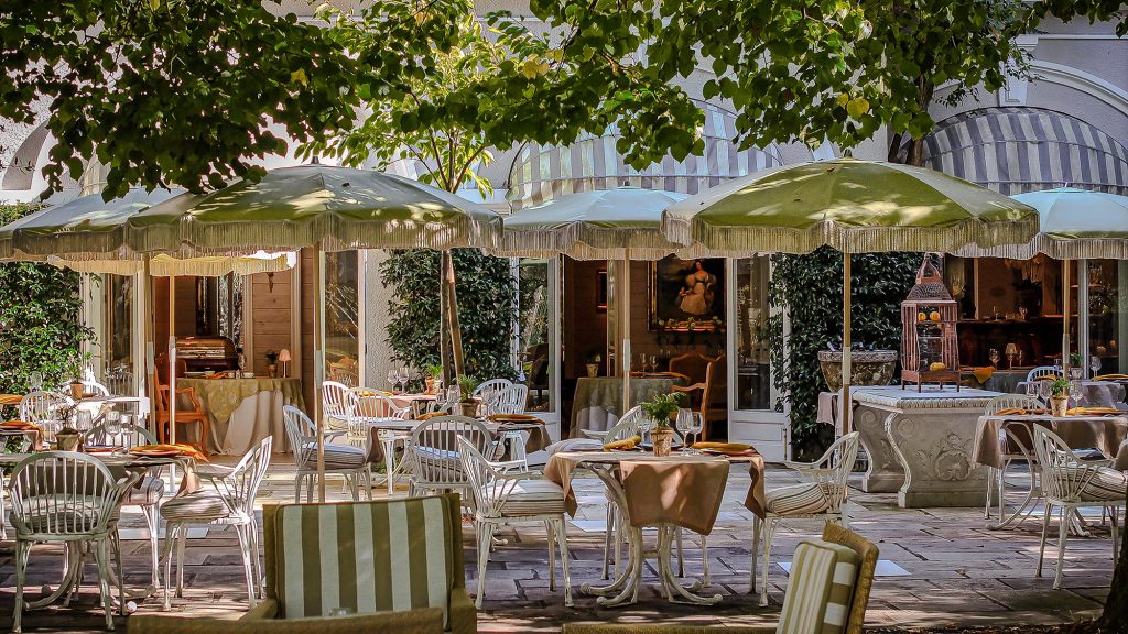 The sun-dappled terrace at L'ORangerie restaurant of Les Prés d’Eugénie – Relais & Châteaux. A refined setting for al fresco dining in the heart of the estate.