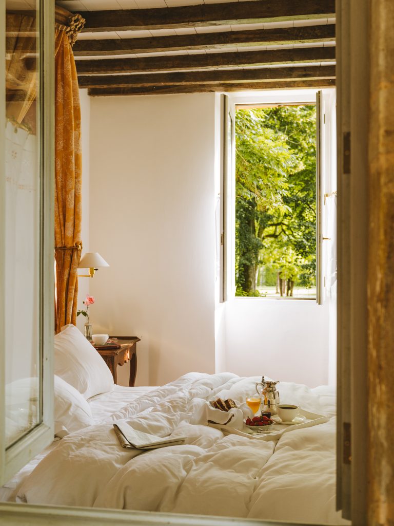 Chambre du Couvent avec poutres apparentes, lit douillet et vue sur un jardin luxuriant.