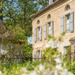 Façade du Logis des Grives avec volets bleu-gris, pierre ancienne et jardin fleuri.